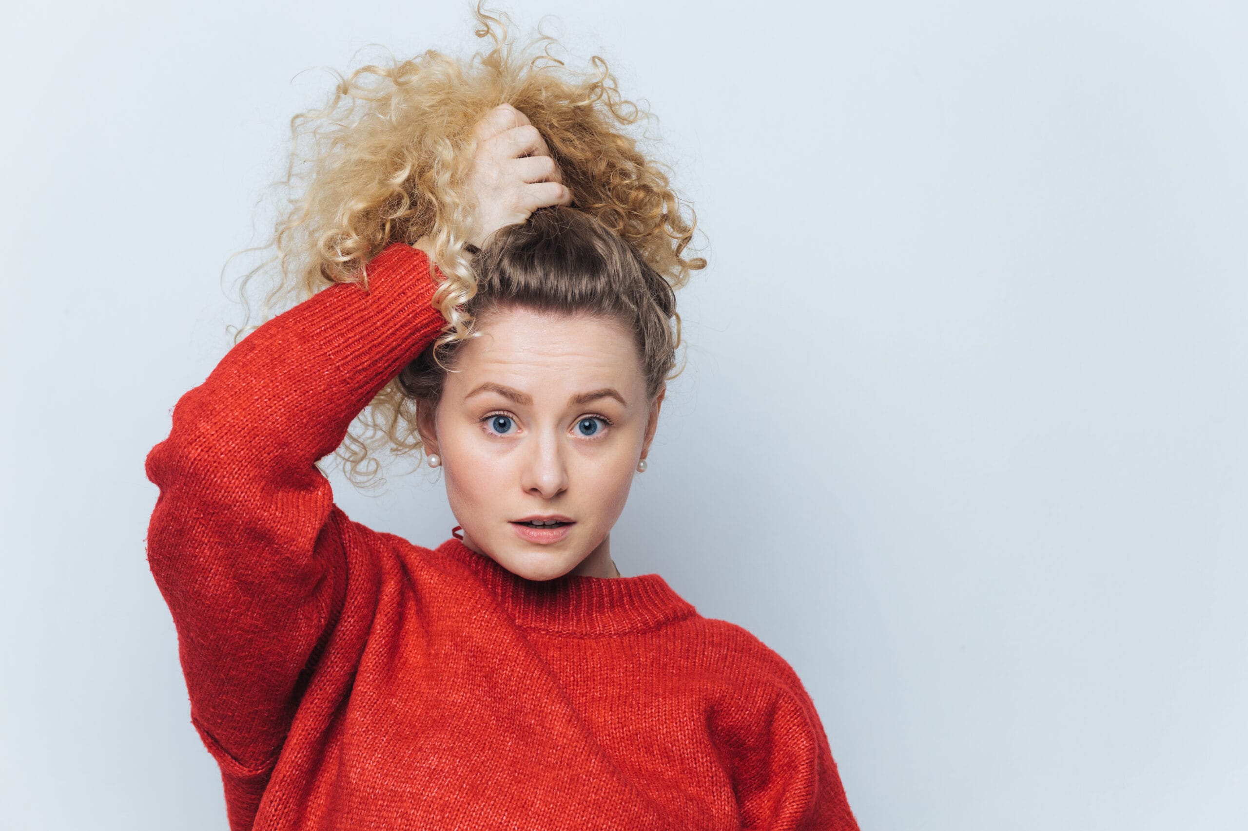 Indoor shot of beautiful blue eyed female in red sweater, poses with stunned expression, dressed in red sweater, isolated over white background. Wondered young woman doesn`t believe in something